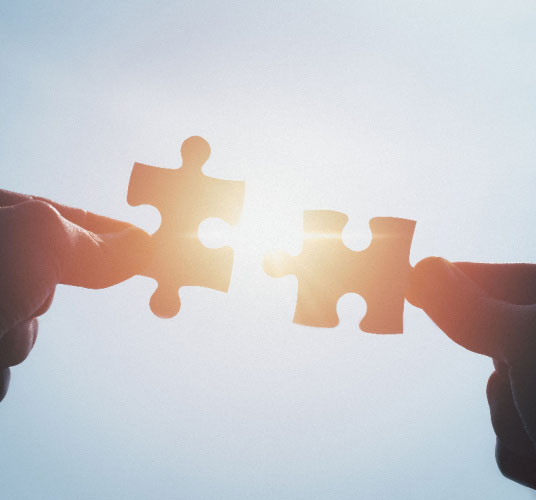 Two hands trying to connect puzzle pieces with sky sunset background